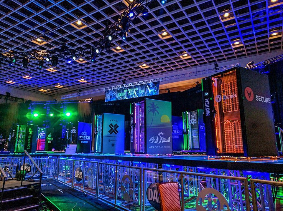Racks de servidores iluminados en azul y verde sobre un escenario durante el Cyber Grand Challenge de DARPA en DEF CON 24